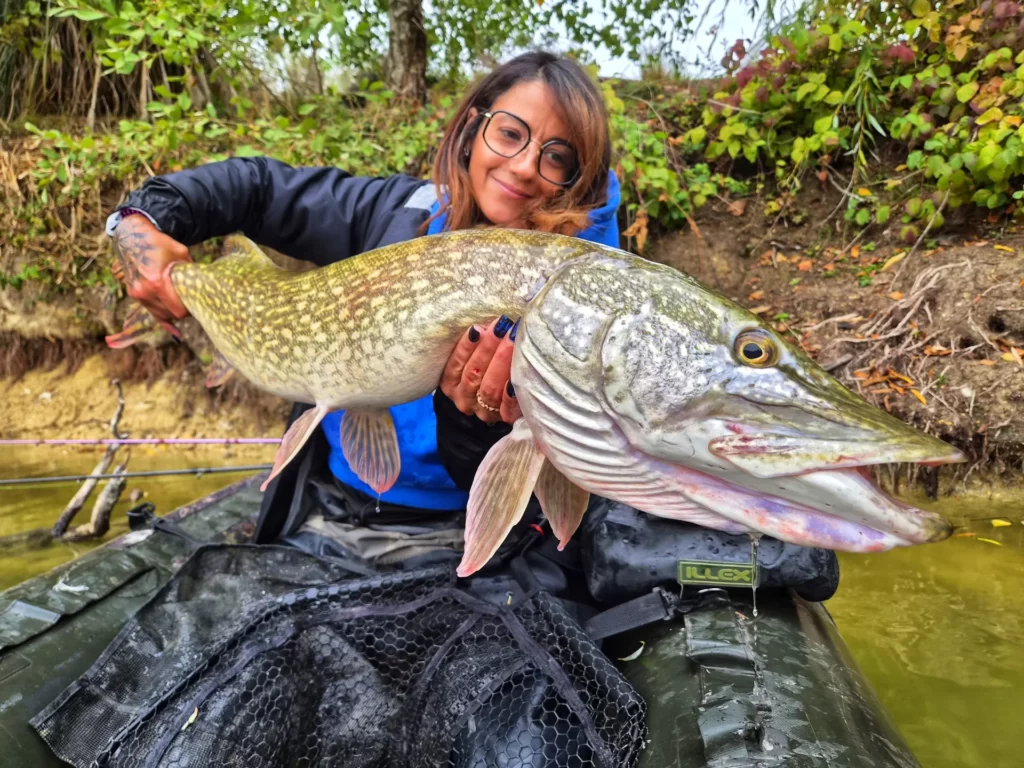 Une pêcheuse présente un brochet au-dessus de l’épuisette de son float-tube.