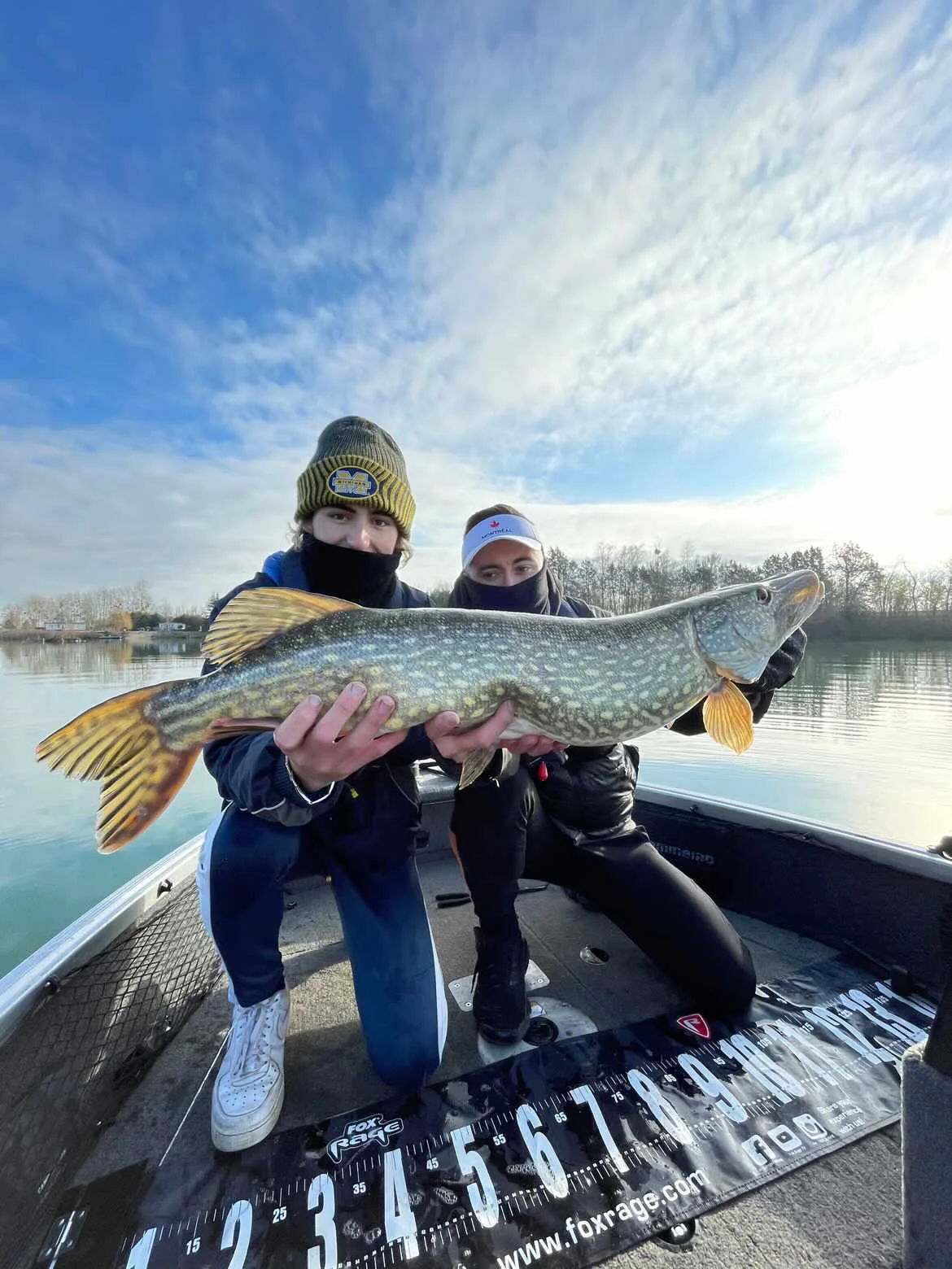 Deux pêcheurs présentent ensemble un brochet à bord d’une embarcation.